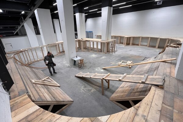 Mann in einer großen Halle, umgeben von Banden und Rampen aus Holz für Skateboards