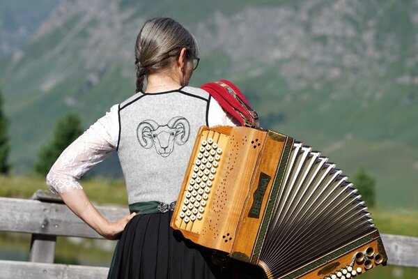 Dirndl mit einem Widderkopf bestickt. Eine Frau trägt eine Ziehharmonika über den Schultern.