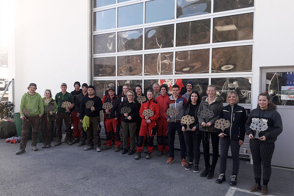 Gruppe Jugendlicher vor einem Garagentor mit Werkstück in Baumform aus Metall in der Hand.