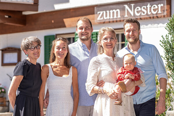 Familienfoto einer Gasthausfamilie. Im Hintergrund ist das Gasthaus in Umrissen zu sehen