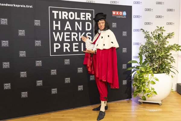 Verkleideter Mann zeigt auf eine Wand auf dem das Tiroler Handwerkspreis Logo abgebildet ist