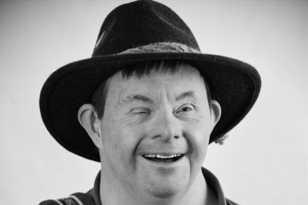 Portrait von lachendem Mann mit Hut und Down-Syndrom