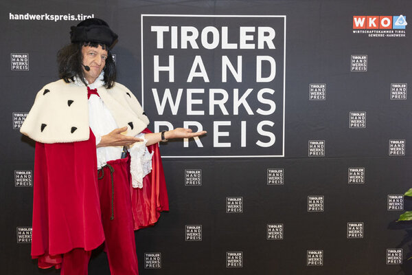 Verkleideter Mann zeigt auf eine Wand auf dem das Tiroler Handwerkspreis Logo abgebildet ist