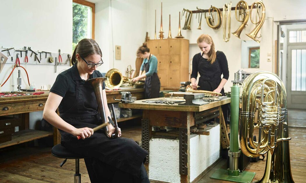 In einer Werkstatt arbeiten zwei Frauen an Blechblasinstrumenten und zeigen handwerkliches Geschick.