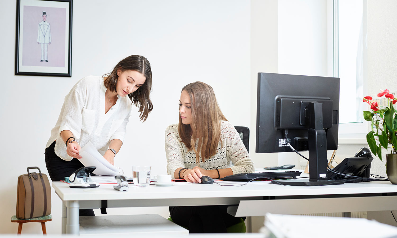 Zwei Frauen am Schreibtisch in einem Büro, die zusammen an ihren Aufgaben arbeiten und sich austauschen.
