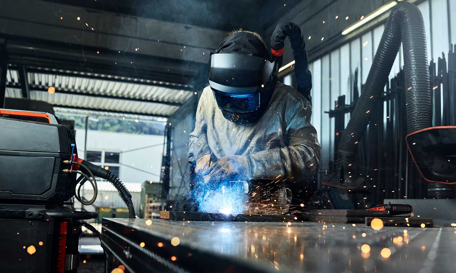 Ein Mann arbeitet in einer Fabrik und schweißt, während Funken um ihn herum sprühen.